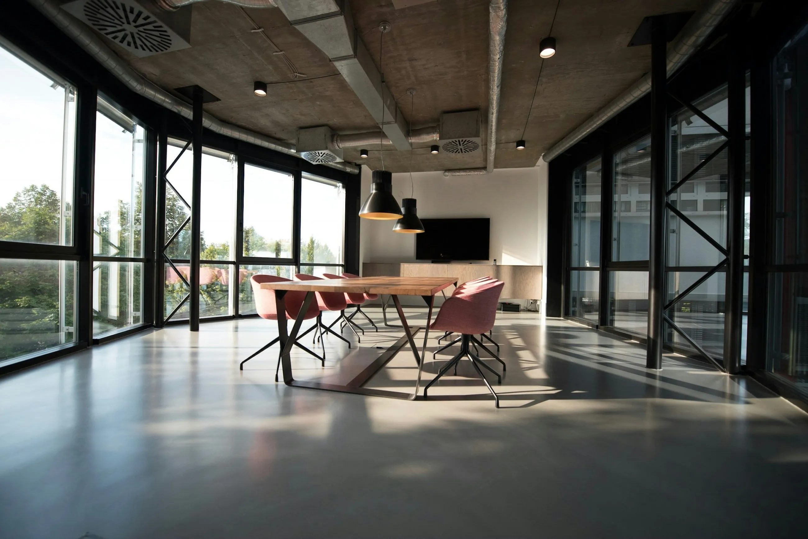 Estudio luminoso con mesa larga de madera y ventanales